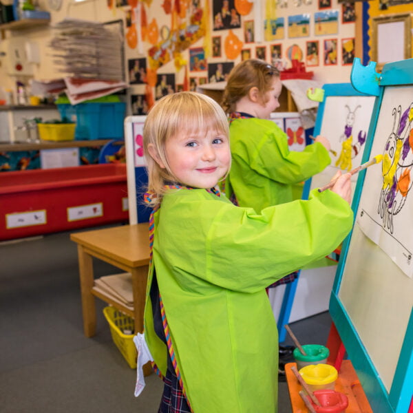 In Nursery, two children are painting pictures on the easels.