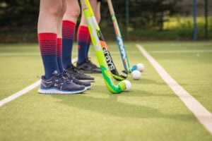 Three hockey sticks and balls can be seen on the Senior School AstroTurf pitch along with three pupils legs.