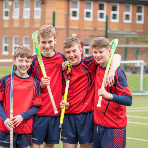 Four boys are stood together in a group holding their hockey sticks on the Senior School Astroturf pitch.