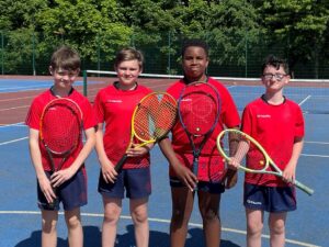 Four pupils are stood together holding tennis rackets. 